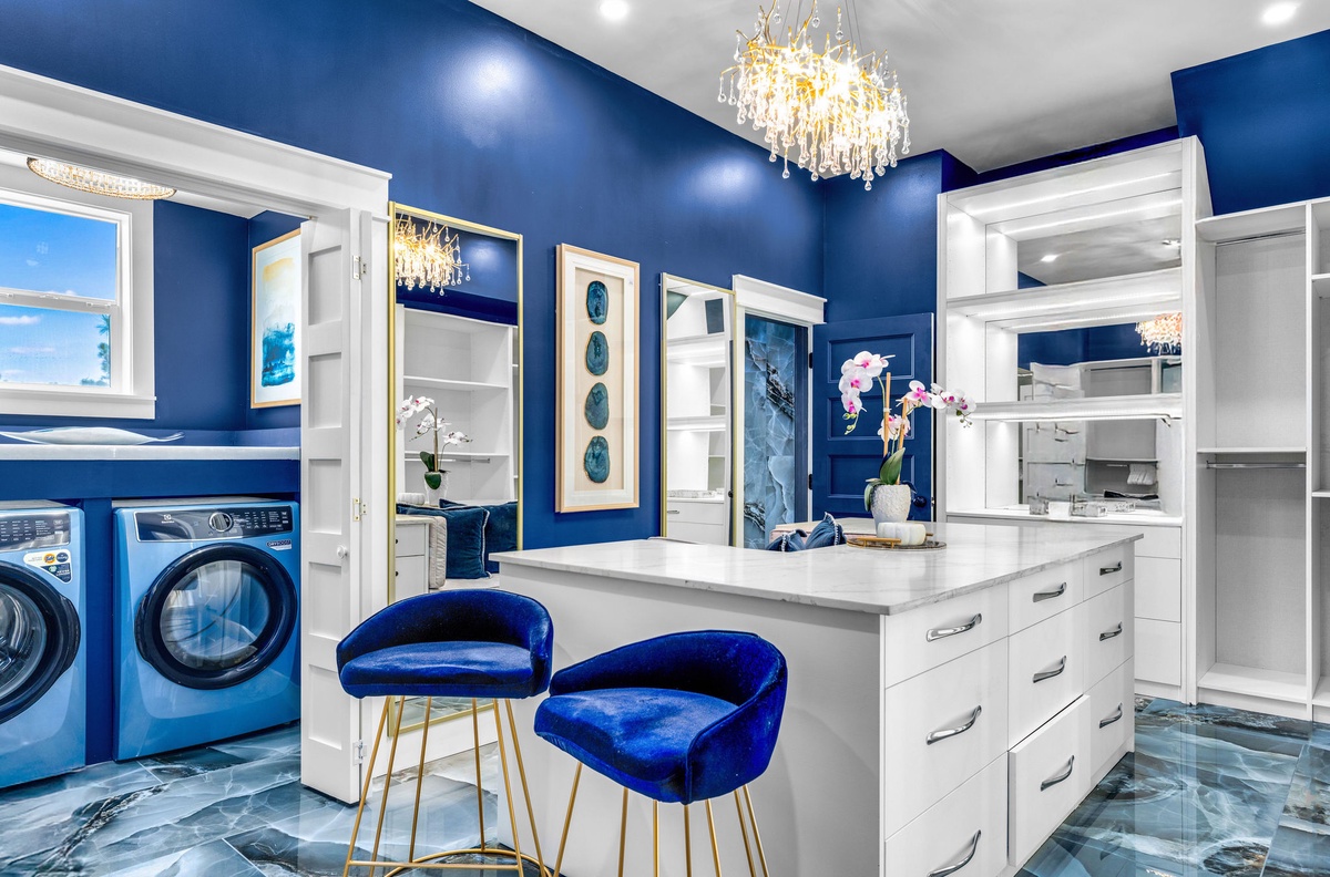 Step into your luxurious closet featuring pristine white cabinetry, plush blue velvet seating, and elegant crystal chandeliers that make organizing effortless.