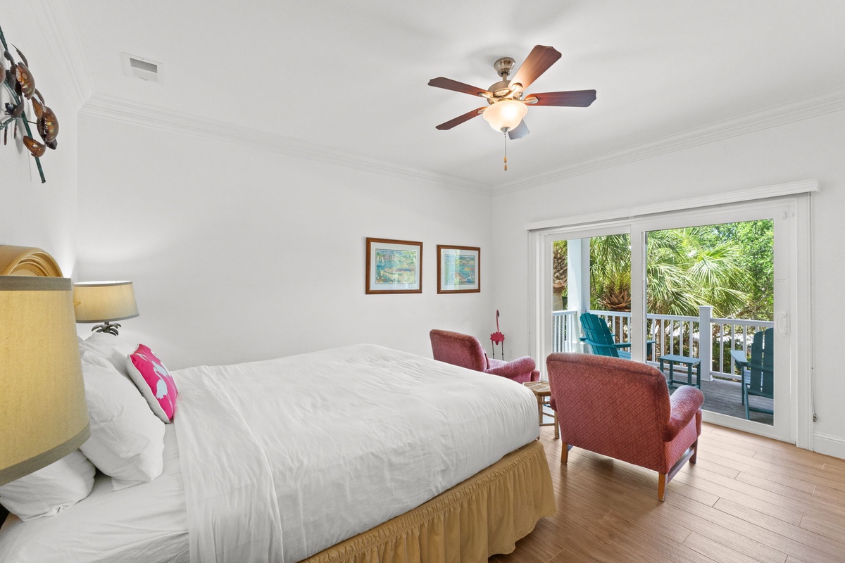 Unwind in your bright, airy bedroom where natural light pours through the doors, leading to your private balcony overlooking lush tropical palms. The gentle ceiling fan keeps things cool as you relax.
