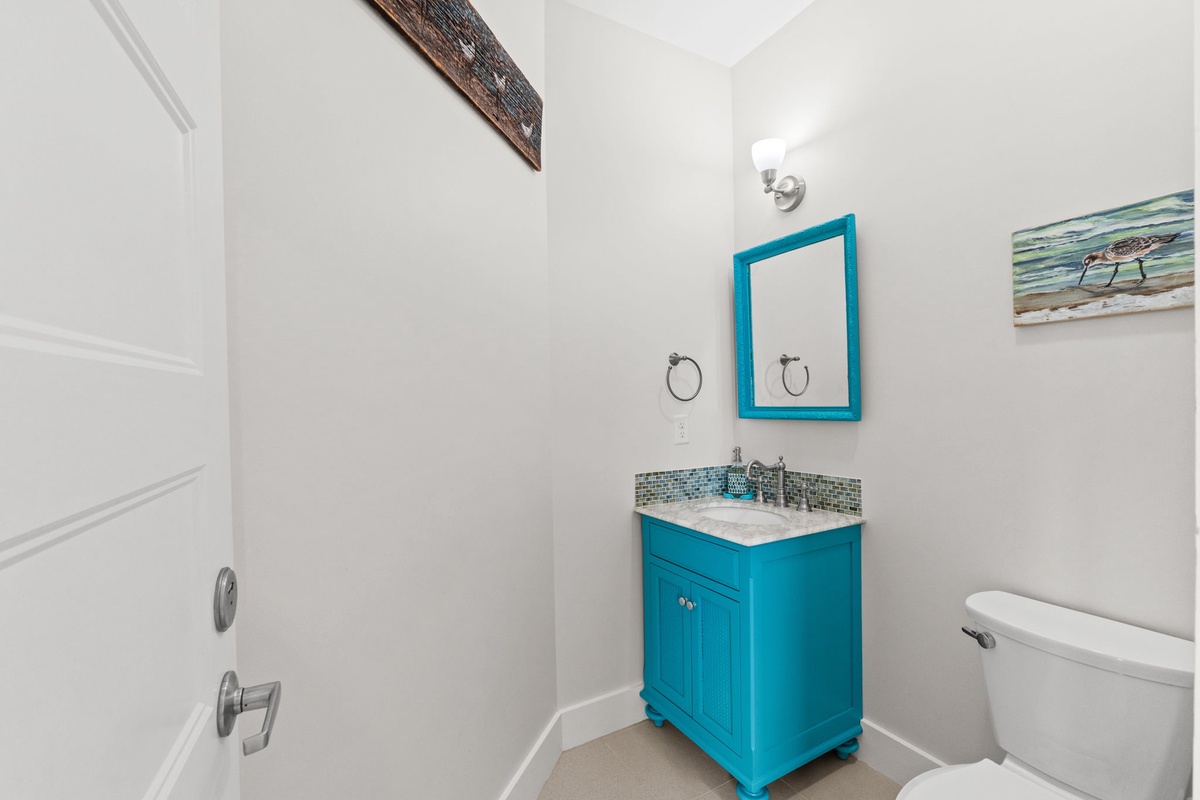 Refresh in this bright bathroom featuring a vibrant turquoise vanity and charming coastal artwork that creates a cheerful, beachy atmosphere.