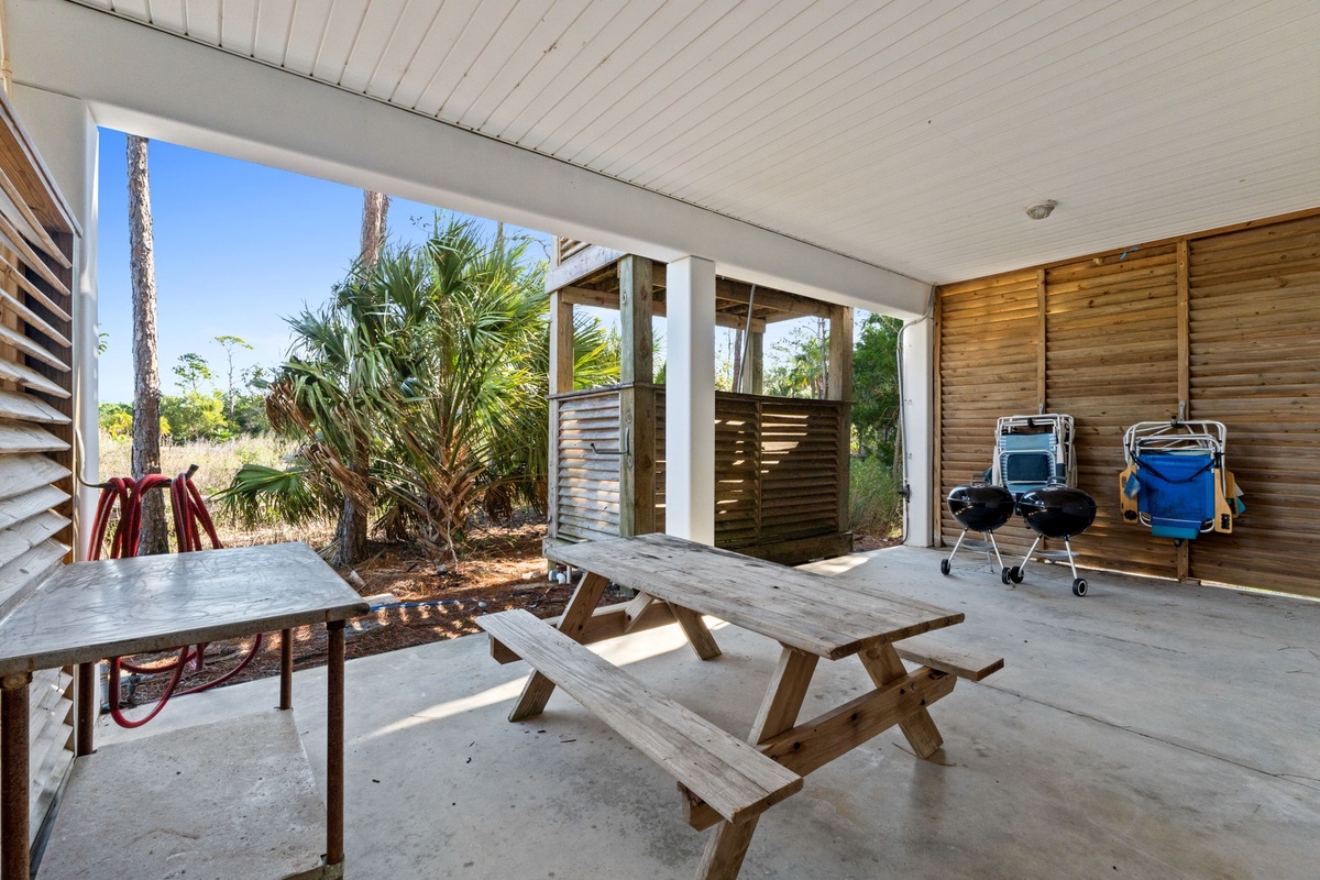 Your covered patio offers shaded outdoor dining with a rustic picnic table, BBQ facilities, and tropical garden views for perfect vacation meals.