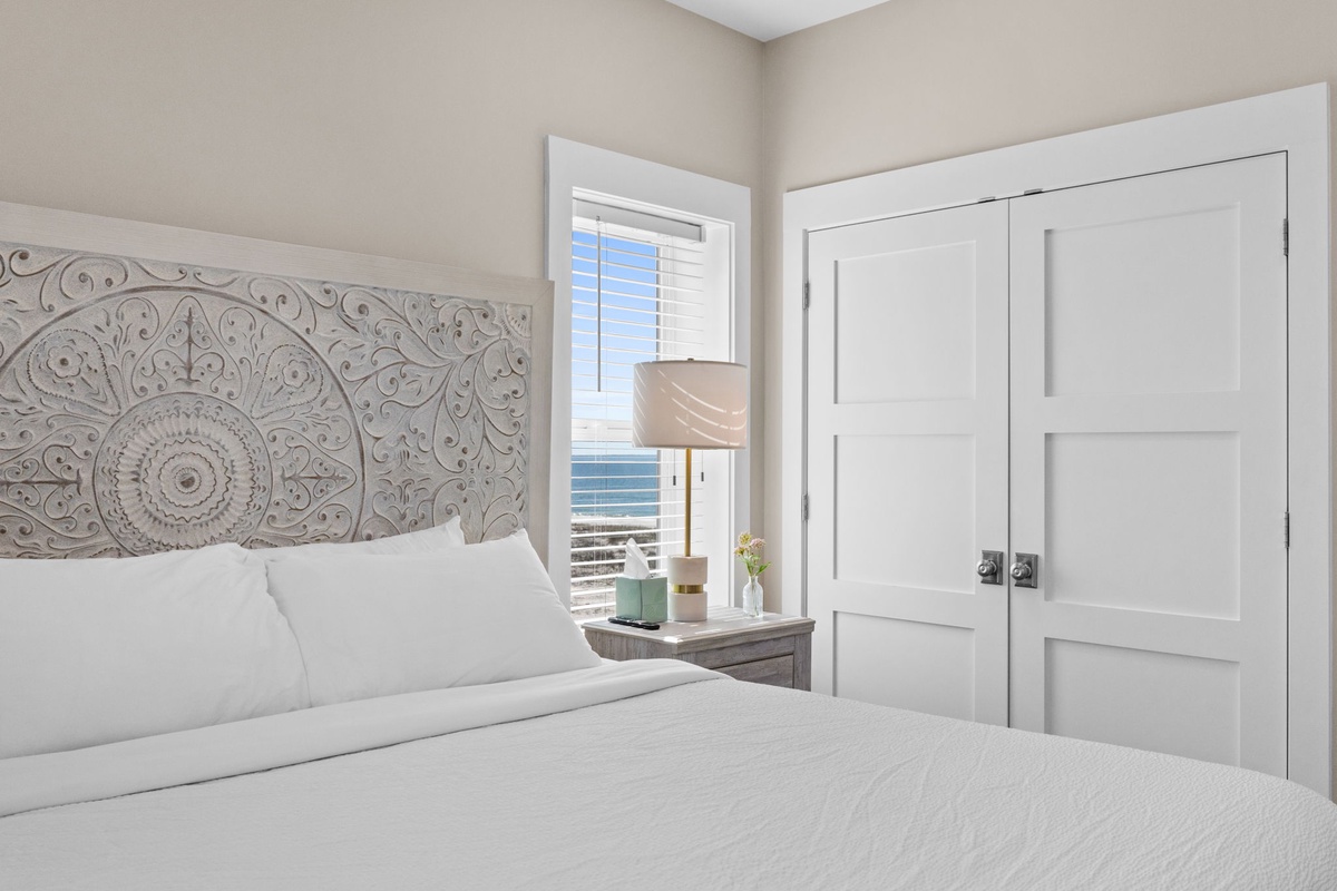 Drift into peaceful sleep beneath the ornate carved headboard, with ocean views and thoughtful bedside touches creating your perfect retreat.