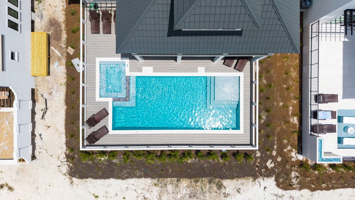 Aerial perspective showcasing the property's outdoor swimming pool, surrounded by modern decking and lounge seating within a residential coastal setting.