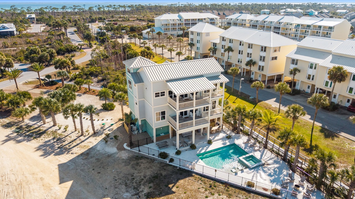 Aerial view of beachfront vacation rental with private pool, surrounded by palm trees and coastal community.