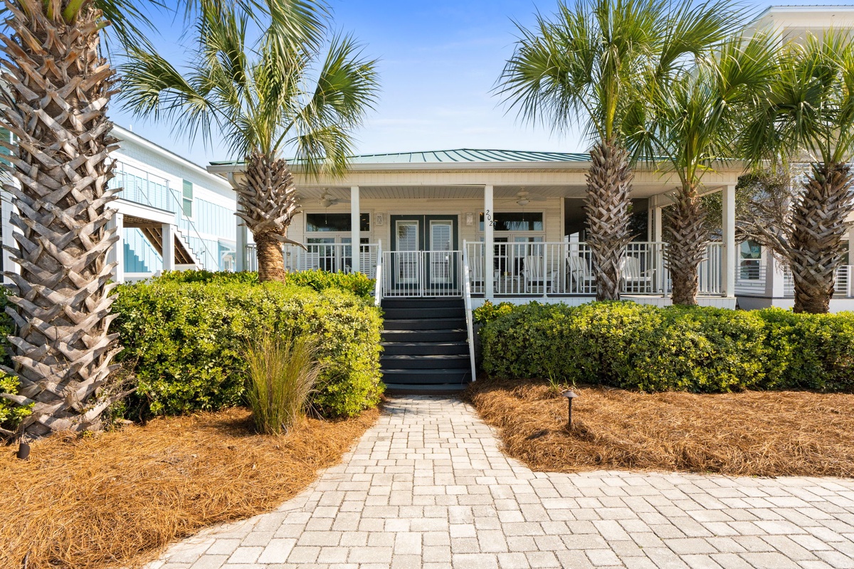 Charming coastal cottage with tropical landscaping and covered porch welcomes guests to their beachside retreat.