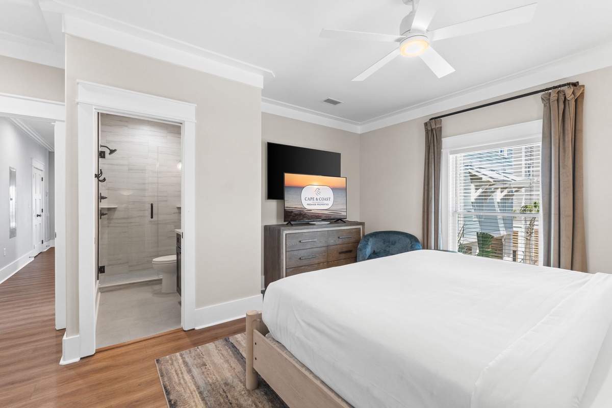 Unwind in your bright, modern bedroom with crisp linens, ceiling fan, and an ensuite bathroom. Natural light floods through the window, creating a serene retreat for restful nights.