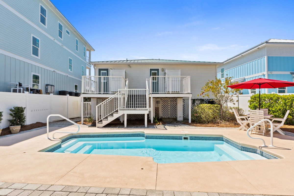 Charming coastal property featuring a private swimming pool surrounded by comfortable beach houses under clear blue skies.