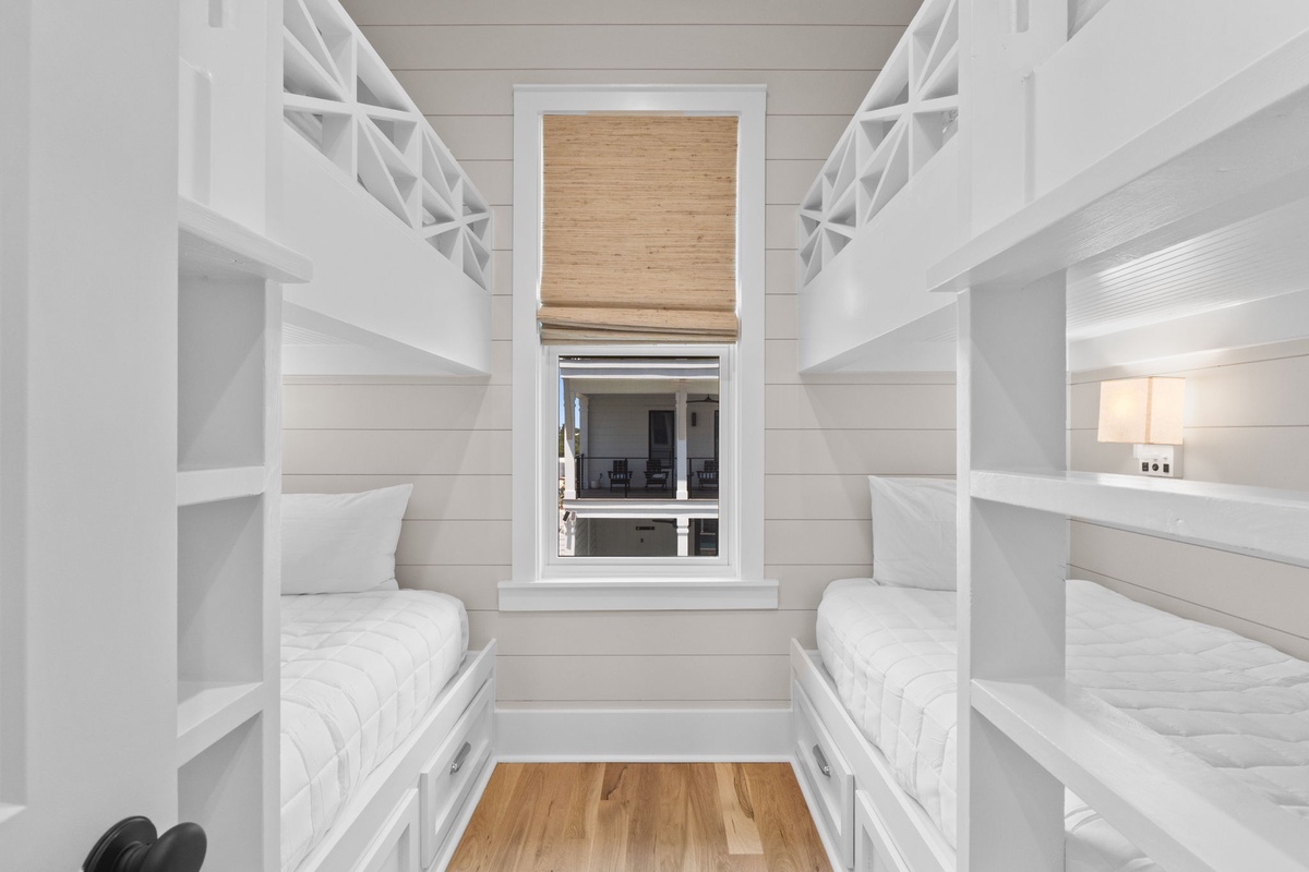 Four cozy bunk beds await, each with crisp white linens and built-in shelving. Perfect for kids or groups, this bright room offers storage and comfort in a charming, space-saving design.