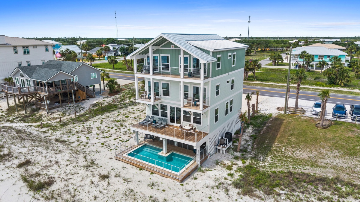 Aerial view of a three-story coastal vacation rental with a private pool, multiple balconies, and palm trees, situated in a beachside neighborhood near the Gulf Coast.