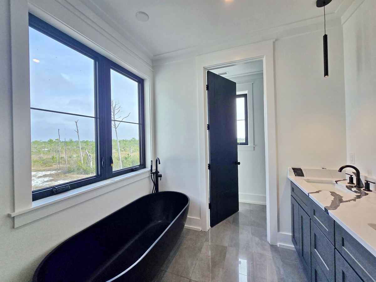 Unwind in your elegant bathroom featuring a sleek black soaking tub perfectly positioned beneath windows overlooking serene natural landscapes.