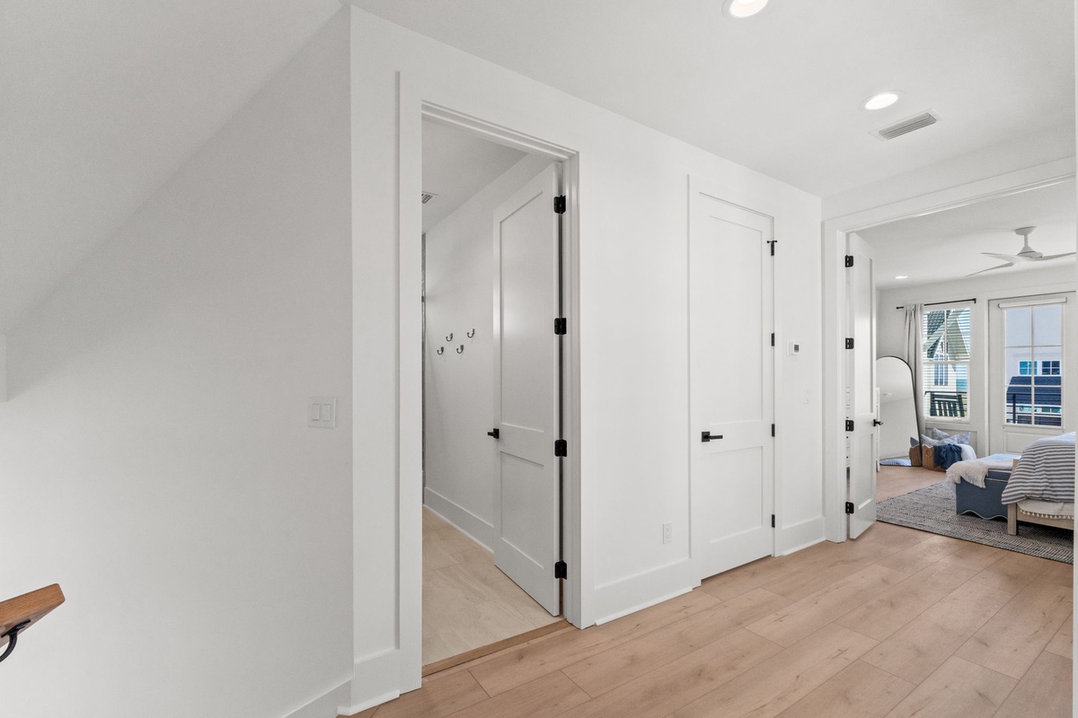 Bright, modern hallway with glass shower door leads to your private bathroom retreat with pristine white walls and warm wood floors.