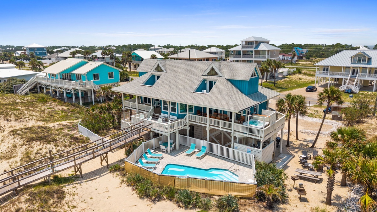 A beachfront neighborhood of coastal homes surrounded by sandy dunes and swaying palms, where this property offers a private pool and easy beach access via a raised walkway.