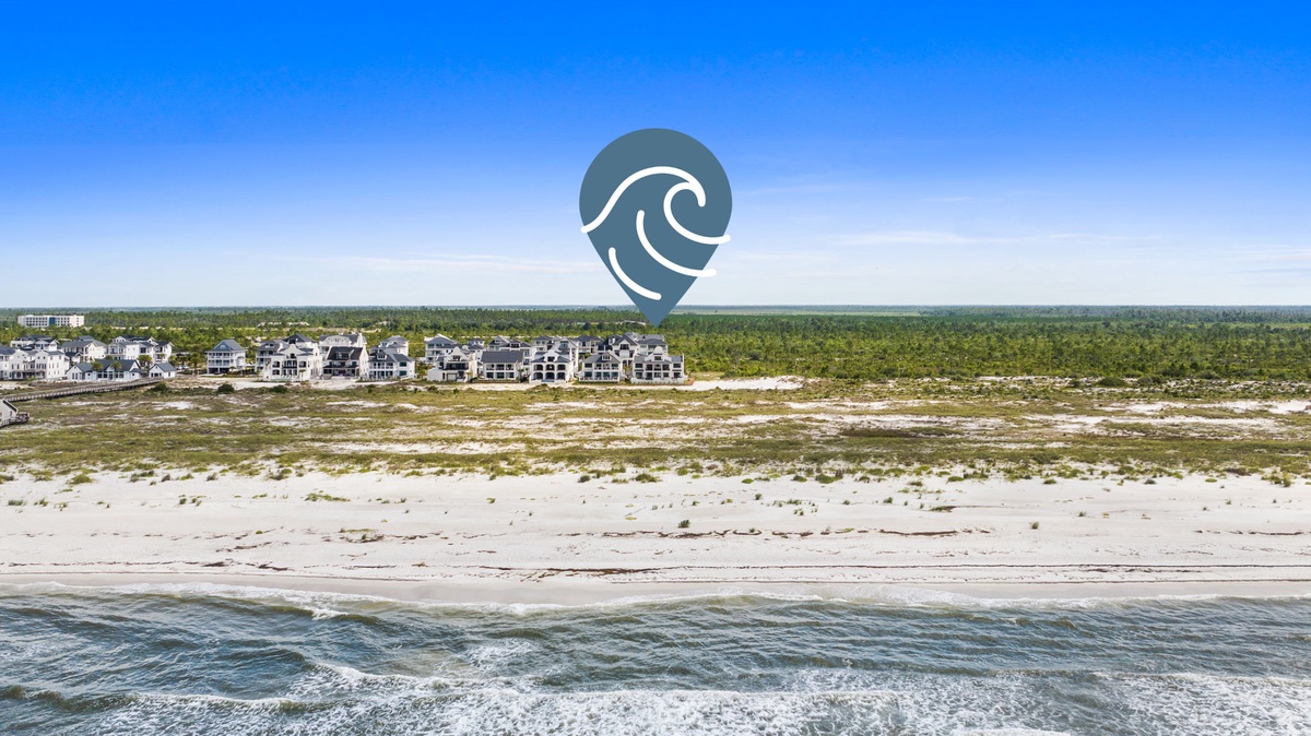 Aerial view showcasing beachfront property nestled between pristine white sand and lush coastal vegetation, offering direct beach access and serene natural surroundings.