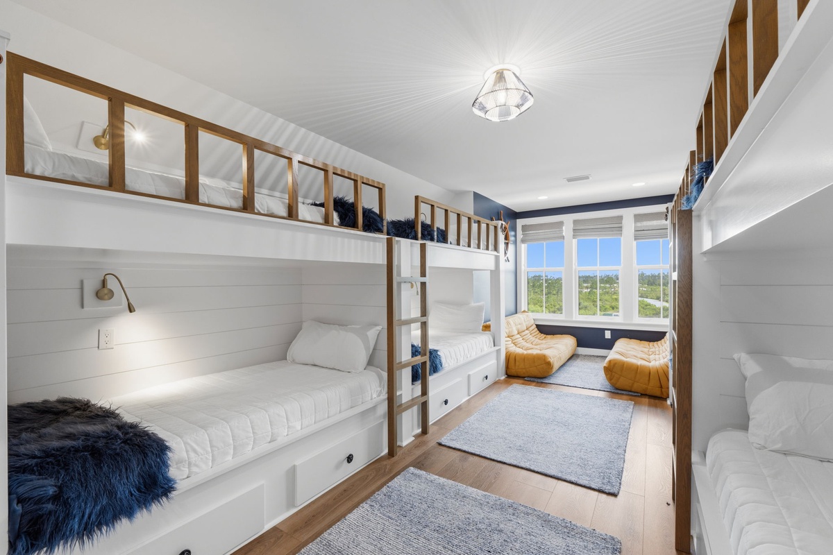 Imagine your group settling into this bright bunk room, where nautical charm meets comfort. Built-in bunks with cozy reading lights, plush poufs, and natural light create a relaxing retreat for all.