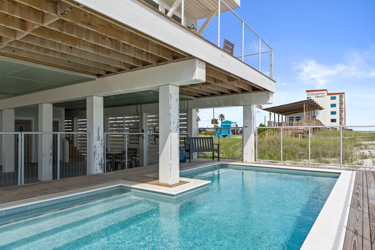 Modern beach house with private pool featuring swim-up seating and rooftop deck overlooking coastal grasslands and neighboring properties.