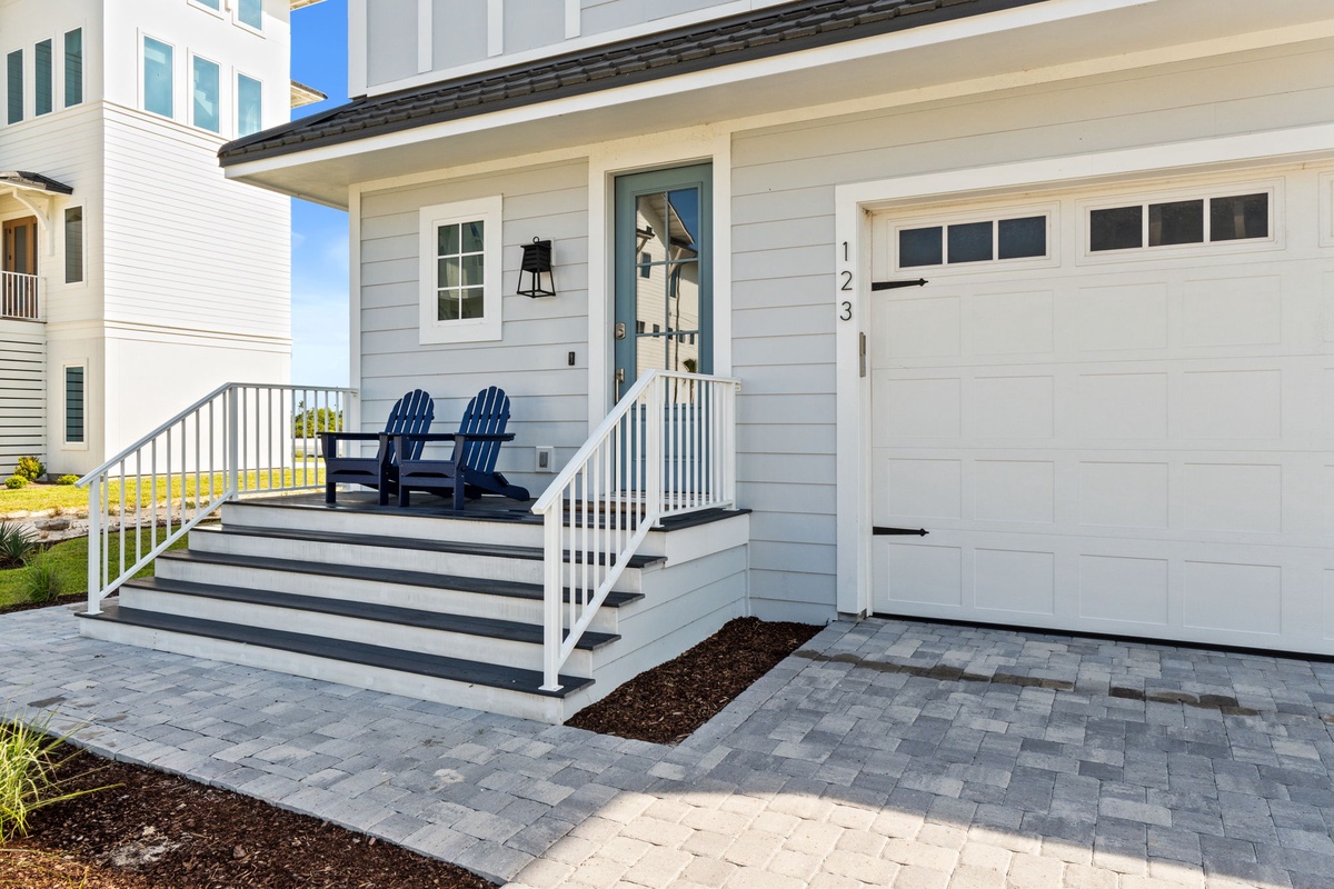 Charming coastal entrance features a classic porch with Adirondack chairs, bright white siding, and easy parking access—welcoming you to your beachside retreat.