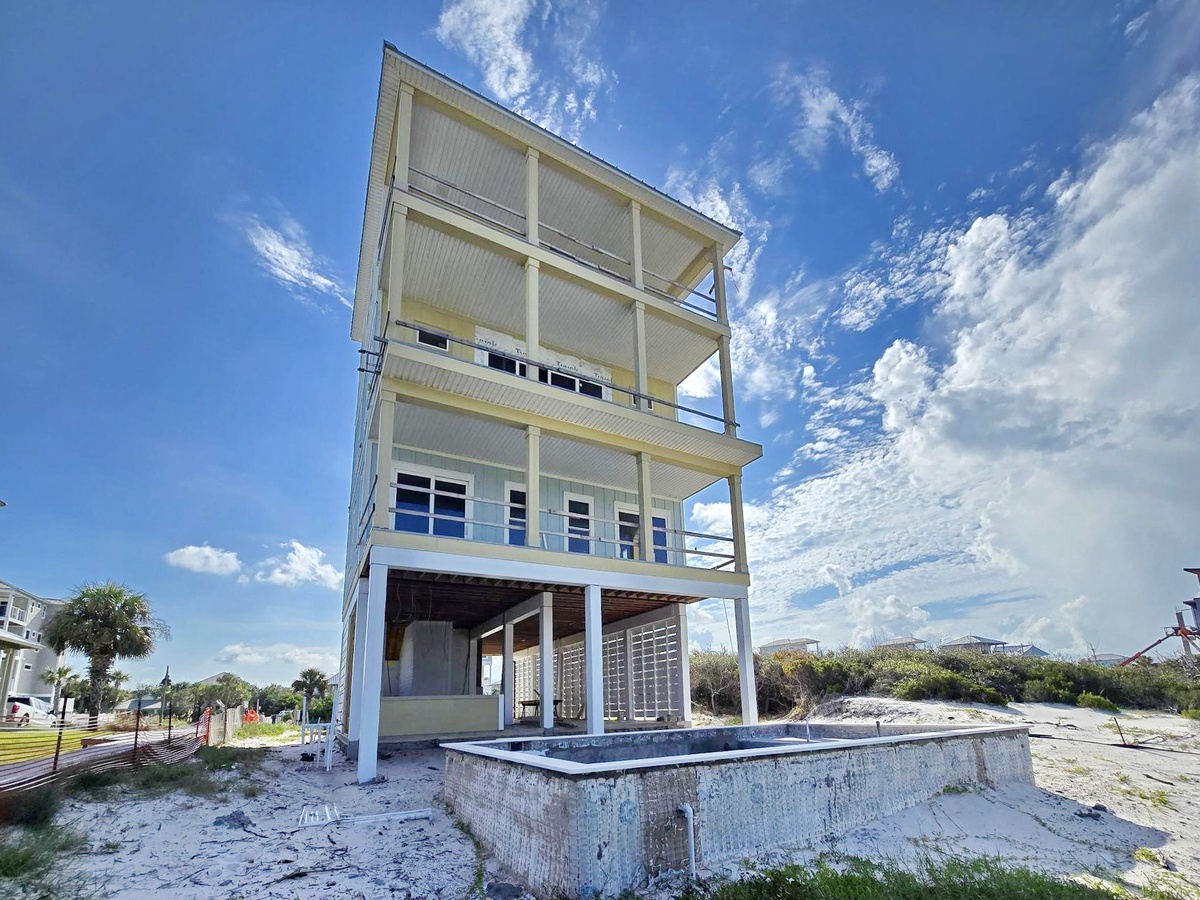 A modern beachfront property with multiple covered balconies and a ground-level pool, offering direct access to sandy shores and panoramic coastal surroundings.