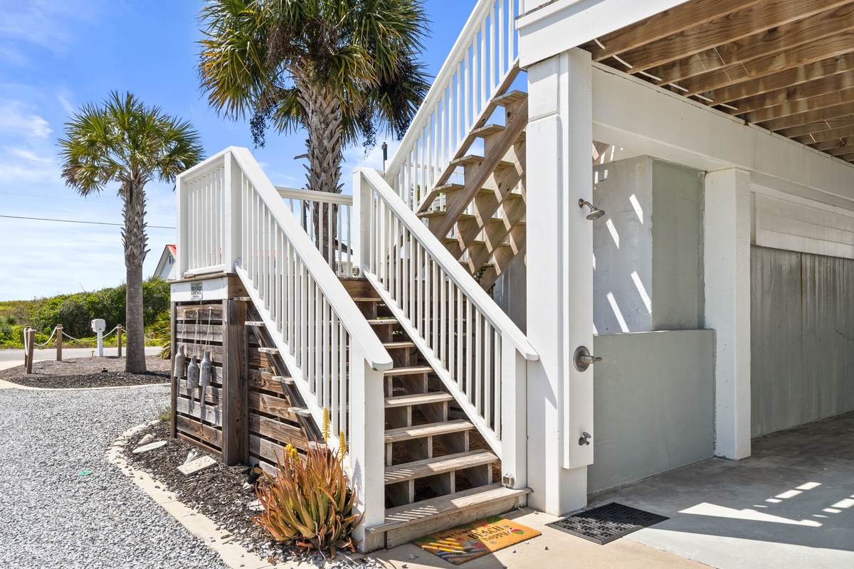 Coastal property entrance features outdoor shower and palm-lined walkways under bright Florida skies.