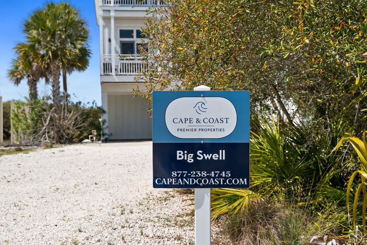 Property entrance sign for Big Swell vacation rental surrounded by tropical palm trees and native landscaping.
