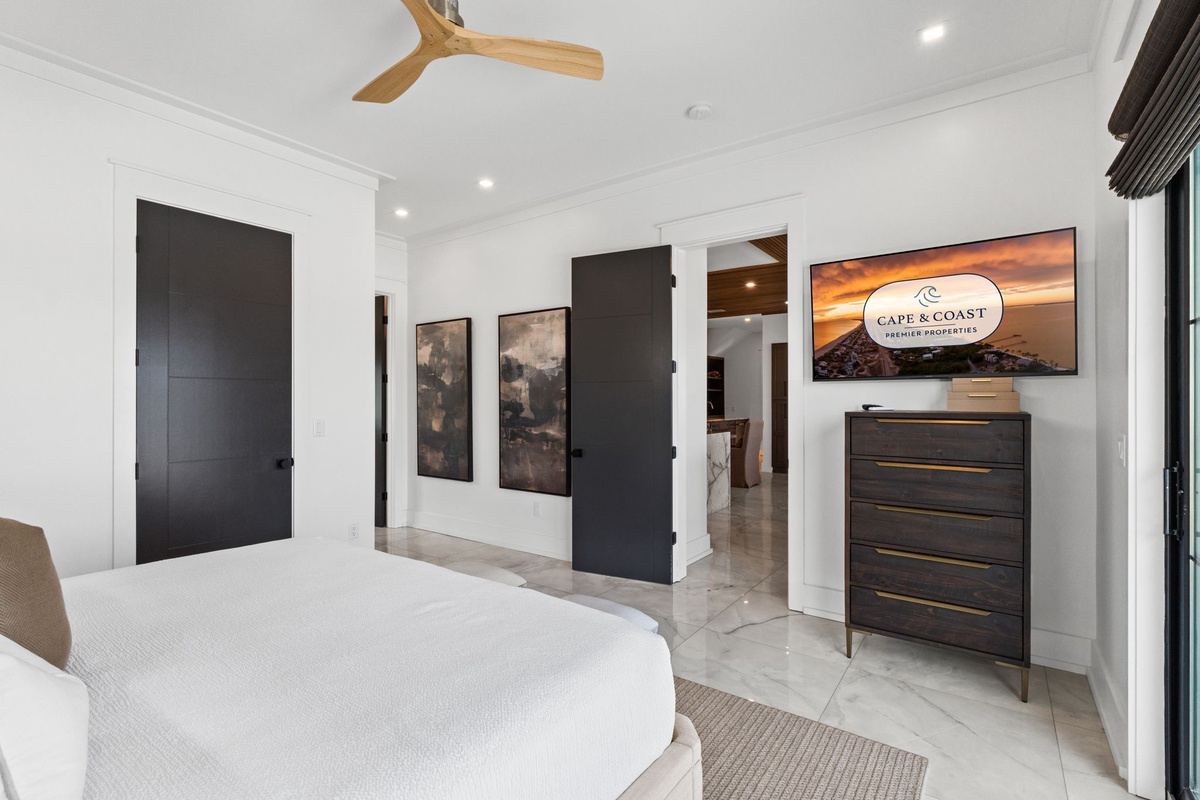 Step into your serene retreat with crisp white walls, elegant tile floors, and a stylish ceiling fan overhead. A dark wood dresser holds your essentials, while artwork adds character to your peaceful sanctuary.