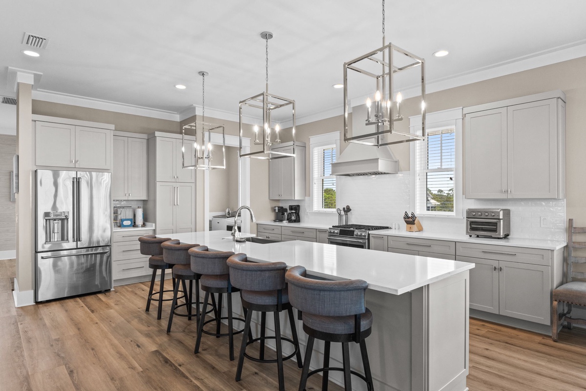 Beautifully designed kitchen with sleek white countertops and soft grey cabinetry. Gather at the spacious island under elegant pendant lights for meals and morning coffee.