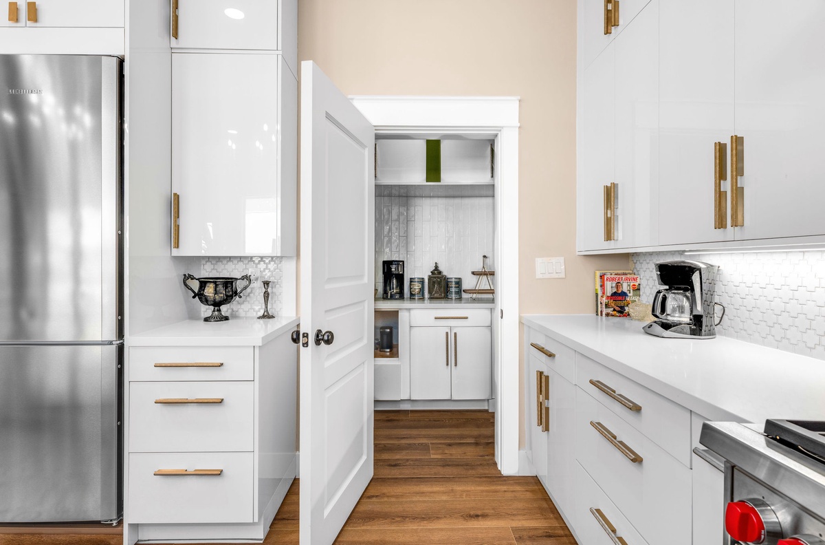 Your gourmet kitchen features gleaming white cabinets, gold hardware, and a coffee station ready for your morning routine.