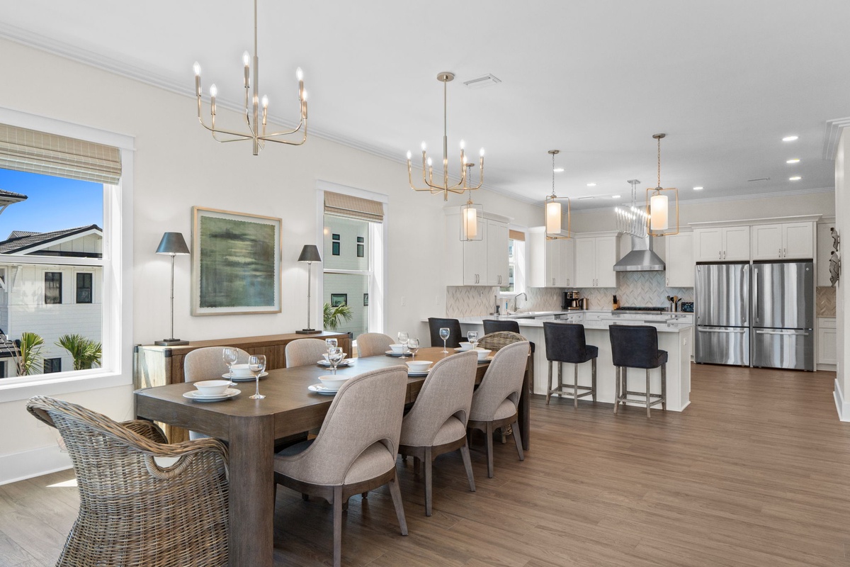 Gather around the spacious dining table and savor meals in this bright, open-plan living space. Elegant chandeliers, modern kitchen with stainless appliances, and warm wood floors create an inviting atmosphere for your group.