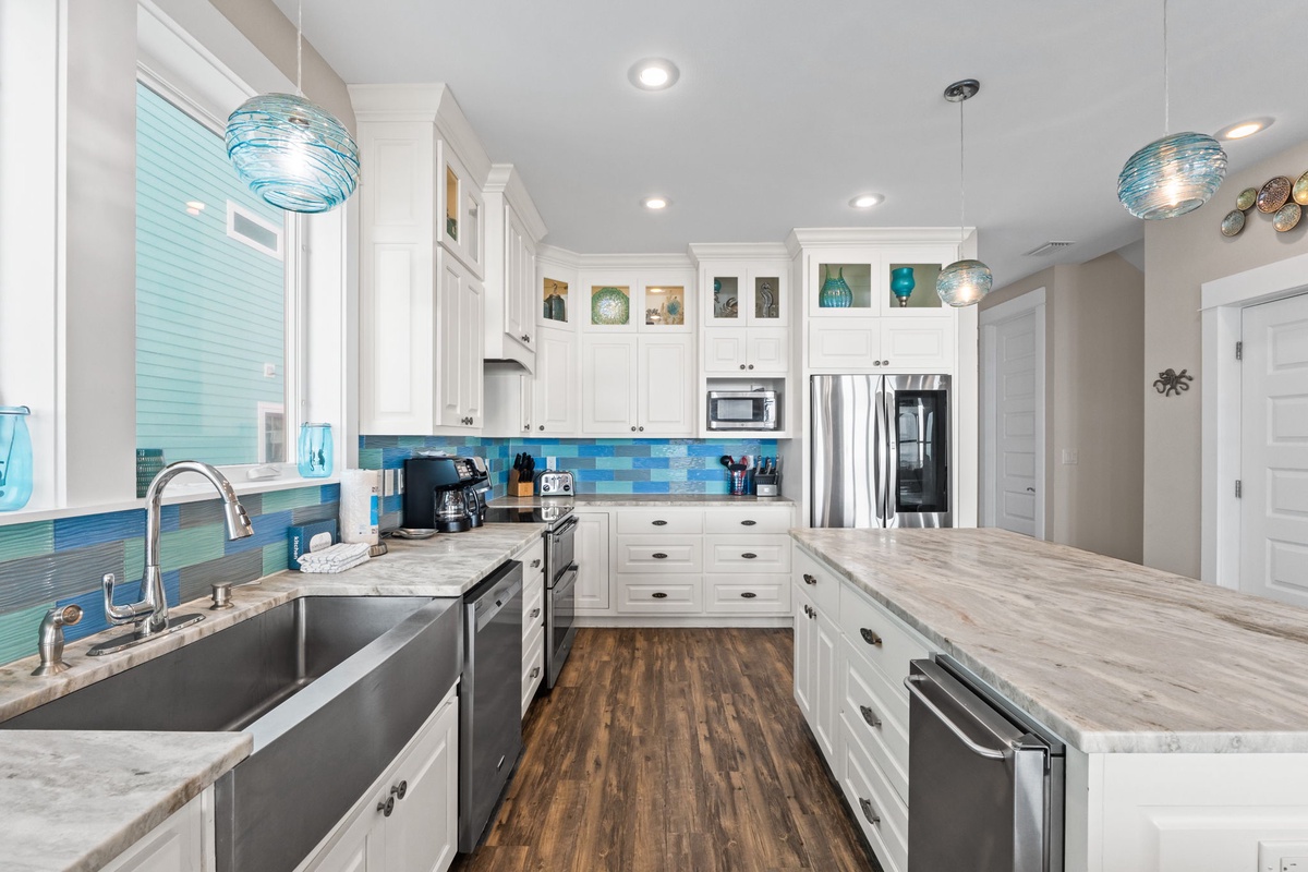 Your gourmet kitchen awaits with stunning blue tile backsplash, marble countertops, and coastal pendant lights creating the perfect culinary retreat.