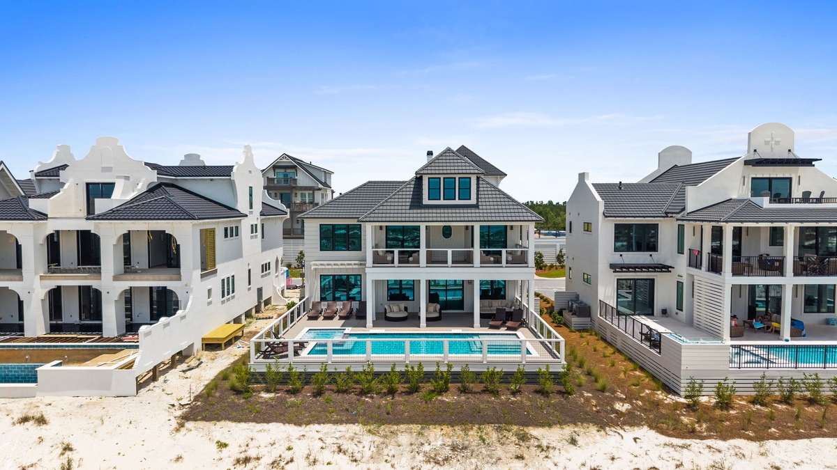 A stunning beachfront residential development features elegant white architecture and private pool access on the sandy shore.