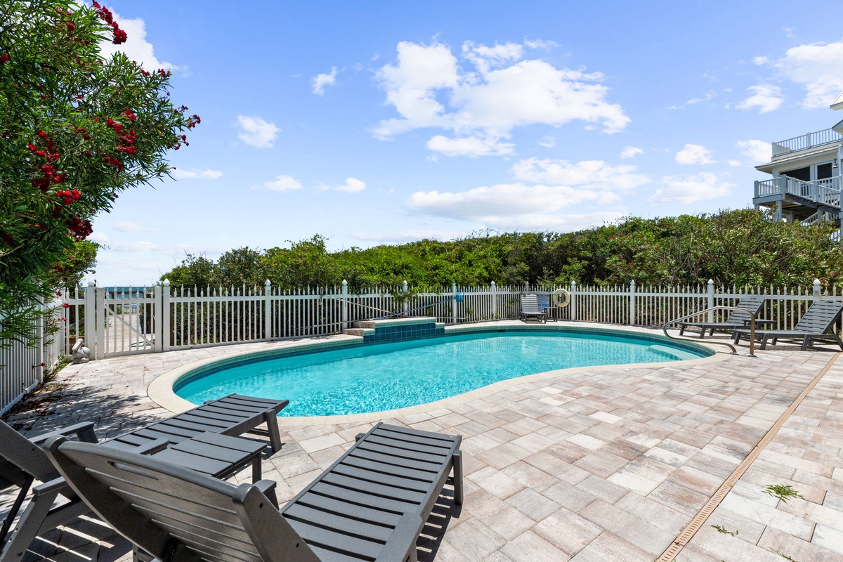 Sparkling pool surrounded by lush greenery and sun loungers, perfect for soaking up the coastal sunshine on a warm afternoon.