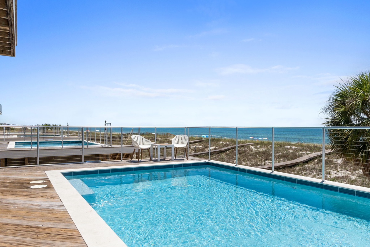 Sparkling pool overlooking pristine beachfront dunes and turquoise waters. Lounge in white chairs, soak up the sun, and enjoy direct access to the sand and surf just steps away.