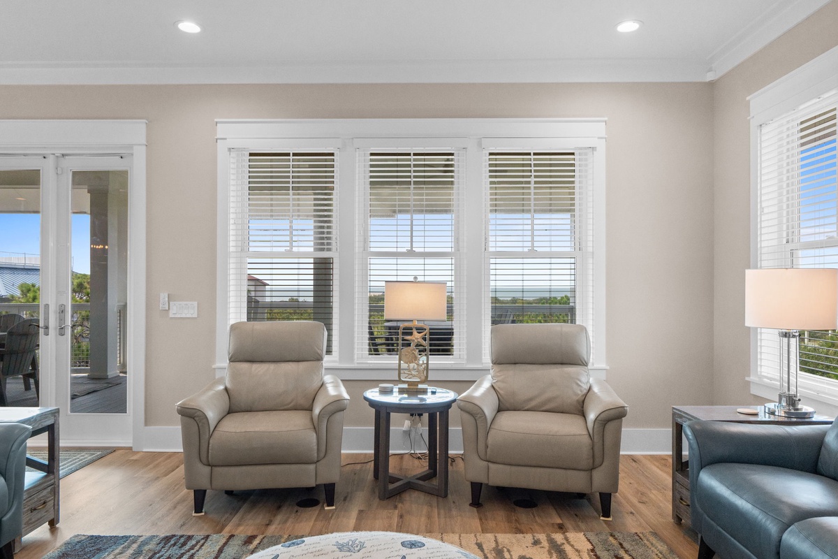 Sink into a pair of plush recliners in this bright, serene living space. Large windows frame peaceful views, while soft neutral tones and polished wood floors create a calm retreat for your mornings and evenings.
