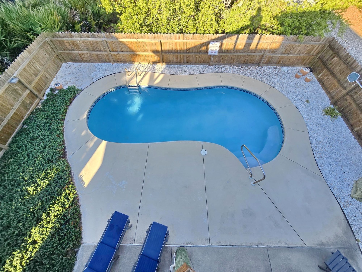 This aerial view shows a kidney-shaped pool surrounded by lush landscaping and a bamboo-fenced patio area on the property grounds.