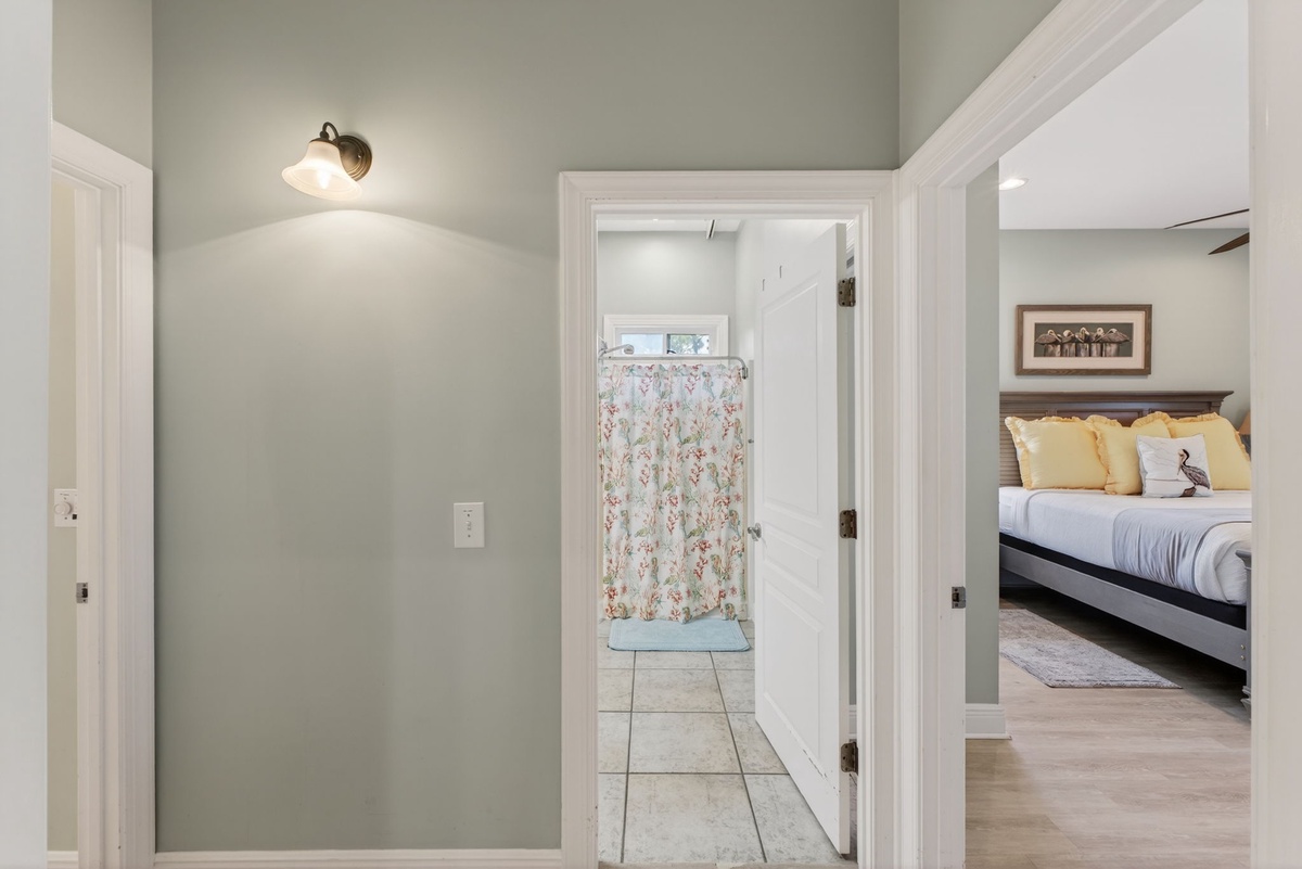 Your private ensuite bathroom awaits through this charming hallway, with floral shower curtains and tile floors creating a cozy, home-like retreat.