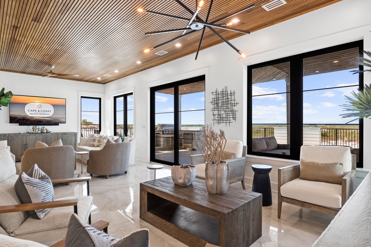 Unwind in this bright, open living room with stunning waterfront views through expansive glass doors. Stylish, comfortable seating and soaring wood ceilings create your perfect coastal retreat.