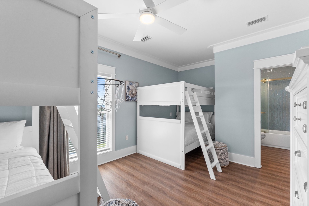 Step into your coastal-inspired bedroom featuring modern bunk beds, warm wood floors, and soothing blue-gray walls. The ceiling fan keeps things cool, while the private ensuite with glass door awaits your relaxation.