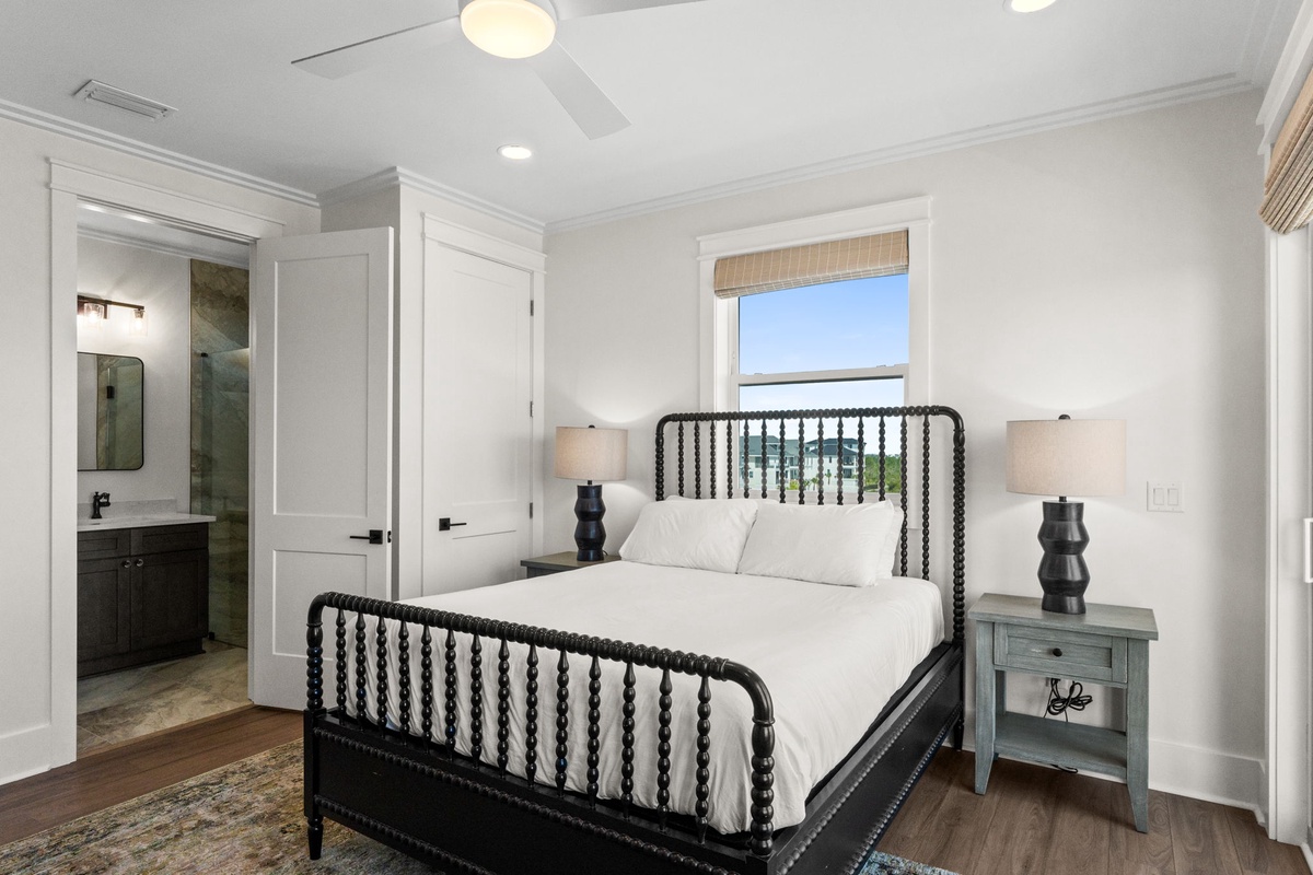 Your peaceful guest room features a stylish bed with classic spindle detailing, soft linens, and an ensuite bath just steps away. Natural light fills the space, creating an inviting retreat.