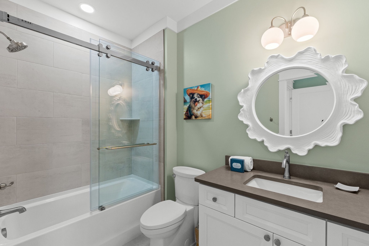 Freshen up in your charming bathroom with soothing coastal vibes, featuring a spacious tub-shower combo and a playful sun-shaped mirror that adds personality to your daily routine.
