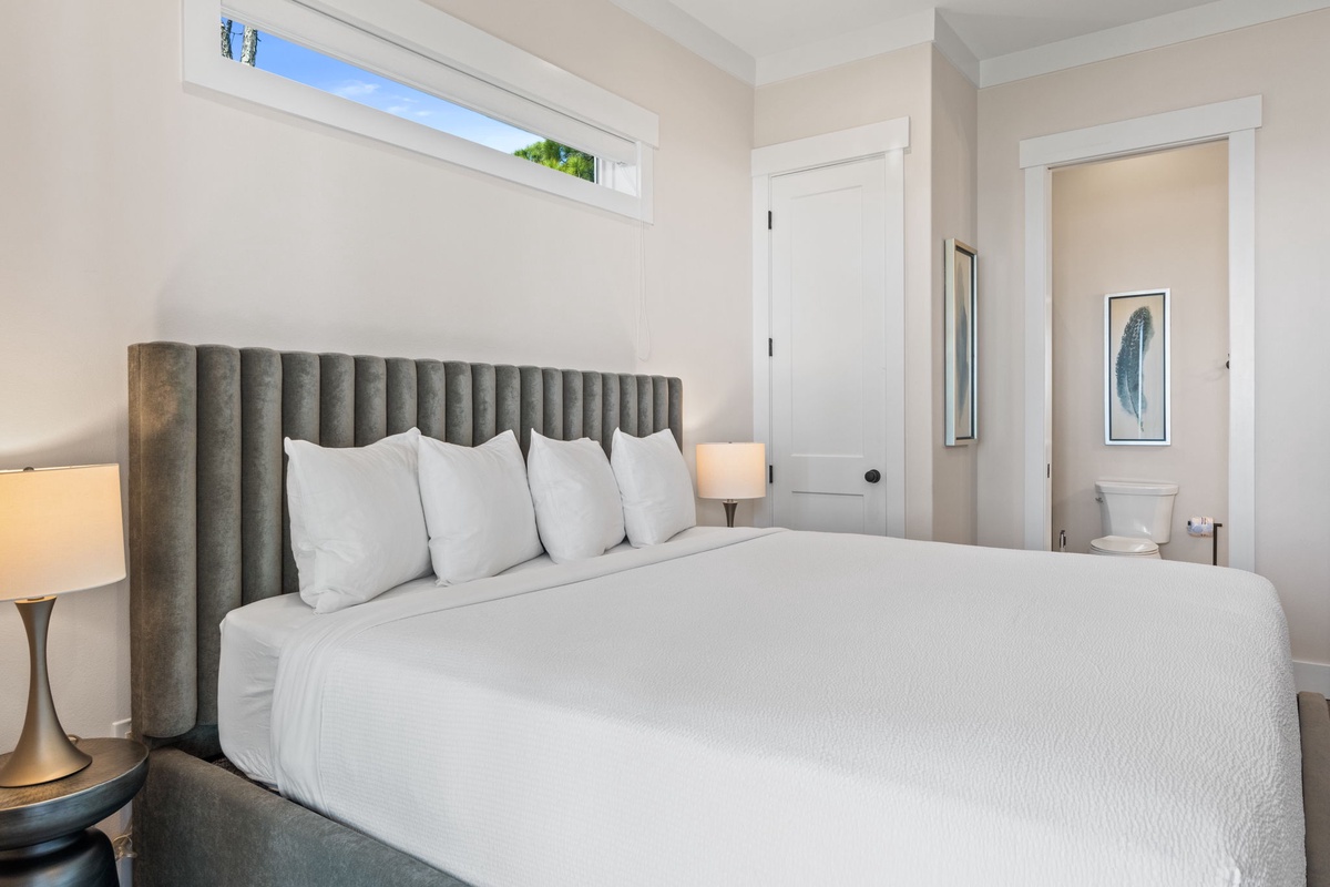 Unwind in your serene bedroom featuring a plush tufted headboard, crisp white linens, and natural light streaming through the skylight above.