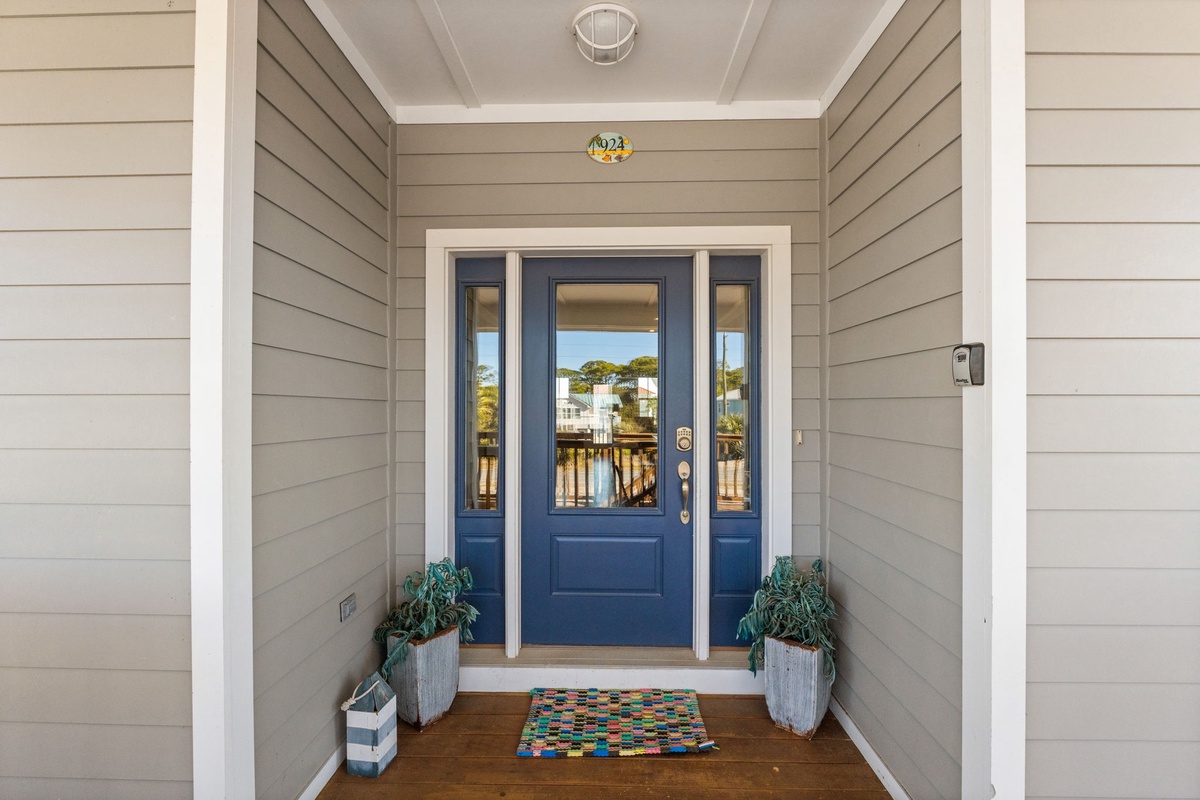 Charming coastal entrance with deep blue door and waterfront views beckoning your arrival to this peaceful retreat.