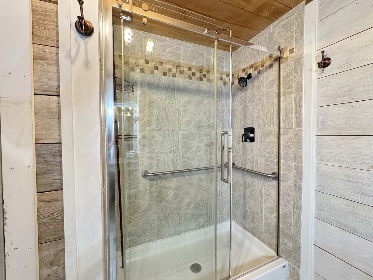 Step into your elegant glass-enclosed shower with beautiful marble-style tiles and convenient grab bars for a safe, luxurious start to your day.