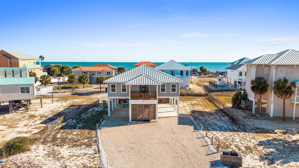 Coastal vacation home community featuring beach houses with metal roofing, situated near pristine turquoise waters and sandy shores.