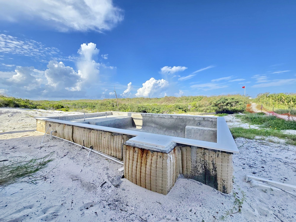A secluded beachside picnic area with concrete tables sits nestled among coastal dunes and native vegetation, offering a peaceful spot to enjoy meals steps from the sand.