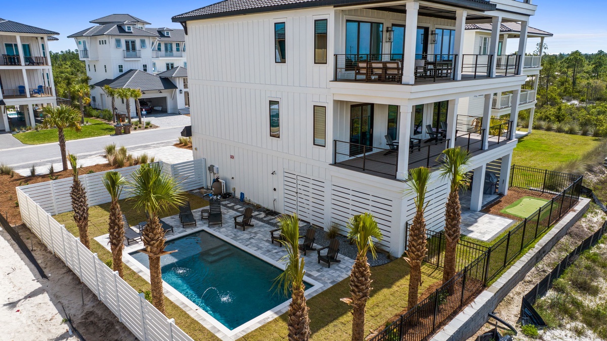 Spacious coastal property featuring elevated balconies with screened porches, a private pool surrounded by palm trees, and expansive outdoor living areas in a quiet neighborhood setting.