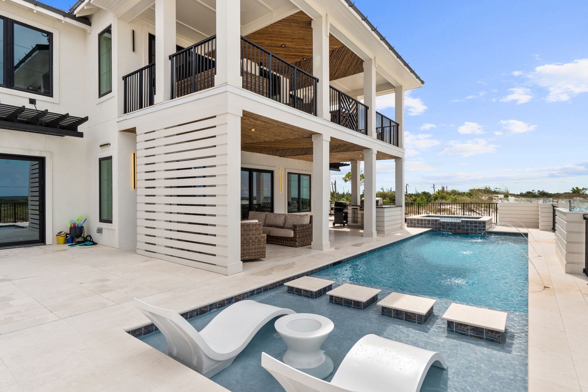 Modern beachside property featuring a multi-level pool with integrated lounge seating, covered entertainment areas with elegant columns, and direct access to natural coastal landscapes.