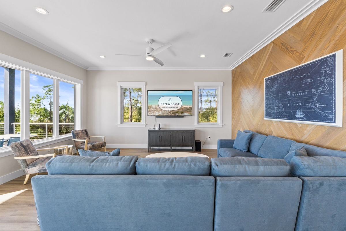 Sink into plush blue seating while natural light fills your spacious living room through expansive windows overlooking peaceful surroundings.