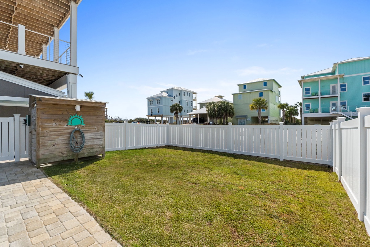 Spacious private backyard with lush green lawn, perfect for relaxing under clear blue skies in this beachside community.
