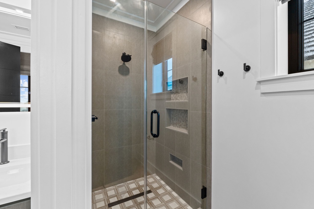 Step into your private spa-like shower featuring elegant beige tile, sleek glass enclosure, and built-in shelving for a luxurious, refreshing experience.