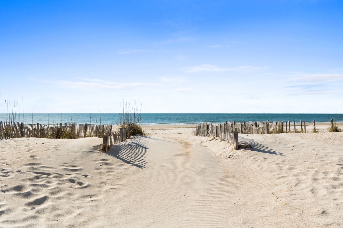 Pristine beach access with wooden boardwalk leading to expansive sandy shoreline and crystal-clear waters.