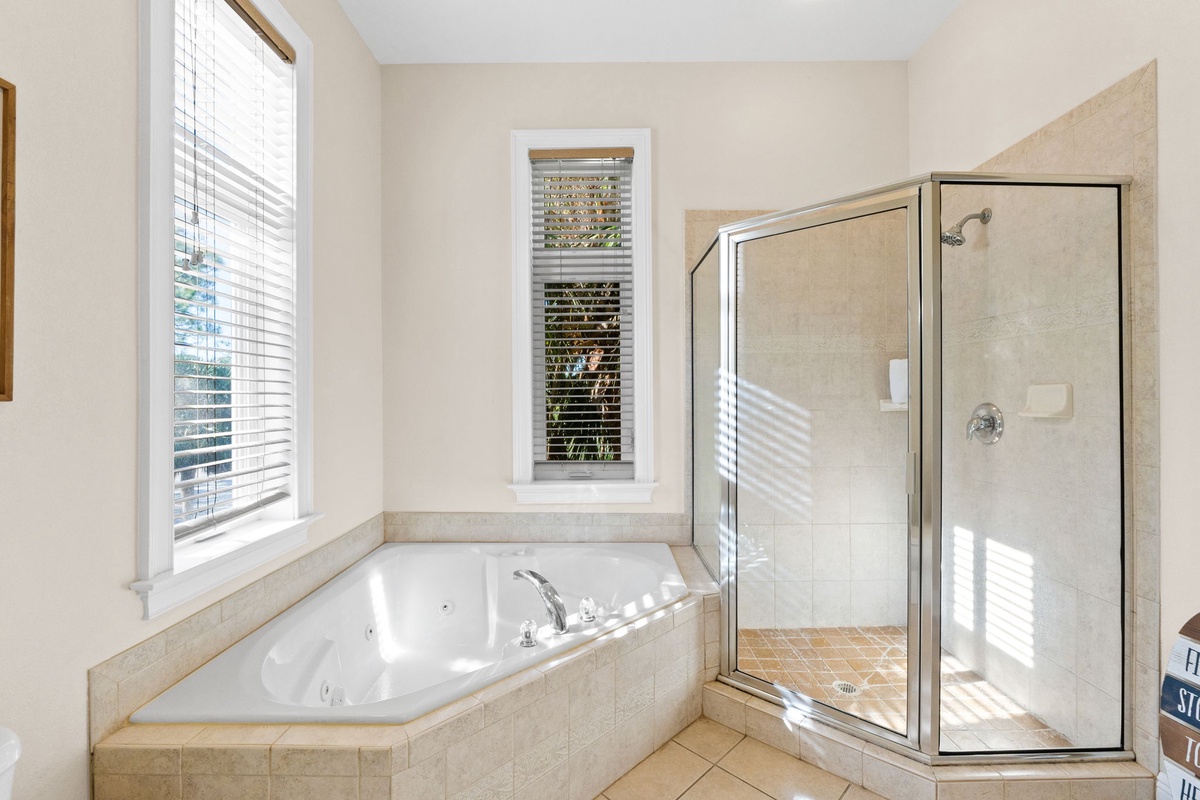 Unwind in your private spa-like bathroom featuring a luxurious corner jetted tub and spacious glass shower, with natural light streaming through.