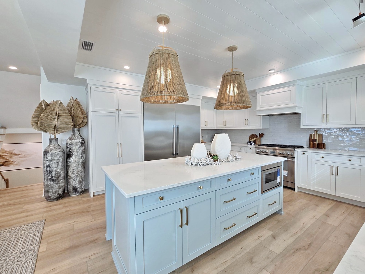 Whip up memorable meals in this stunning coastal-inspired kitchen featuring a spacious island, premium appliances, and stylish woven light fixtures.
